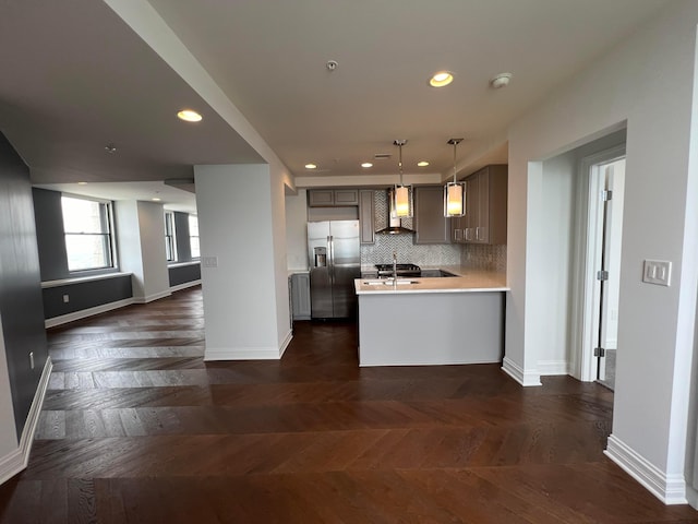 kitchen featuring stainless steel fridge, decorative light fixtures, light countertops, wall chimney range hood, and backsplash