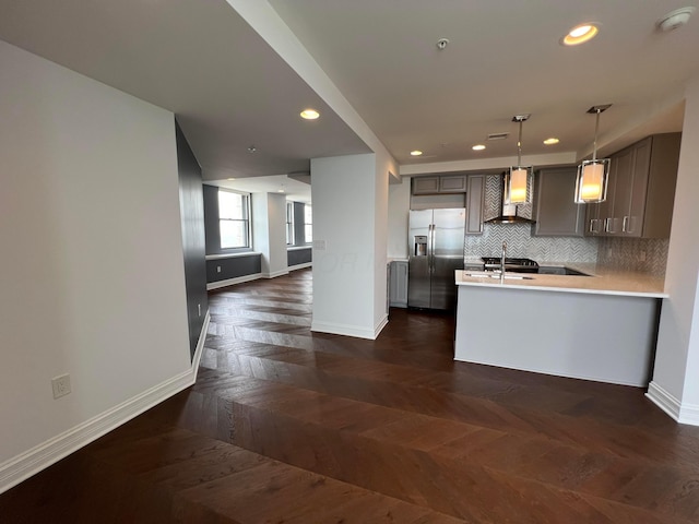 kitchen featuring wall chimney exhaust hood, open floor plan, light countertops, stainless steel refrigerator with ice dispenser, and backsplash