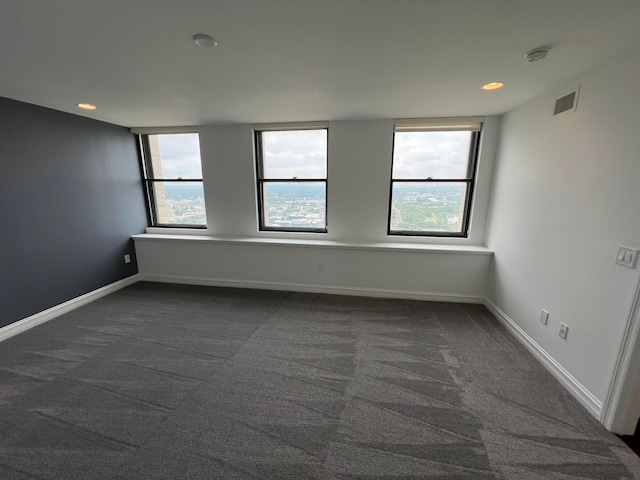 spare room featuring dark colored carpet, visible vents, and baseboards