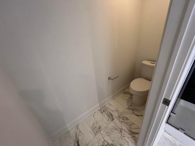 bathroom with toilet, marble finish floor, and baseboards