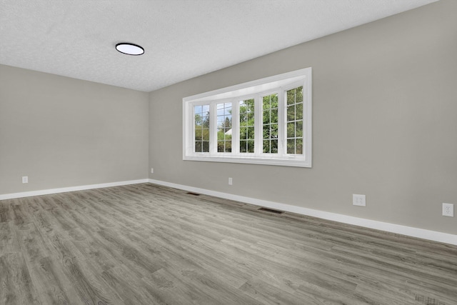 spare room featuring a textured ceiling, wood finished floors, visible vents, and baseboards