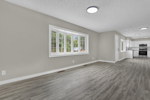 unfurnished living room featuring a healthy amount of sunlight, baseboards, visible vents, and dark wood finished floors