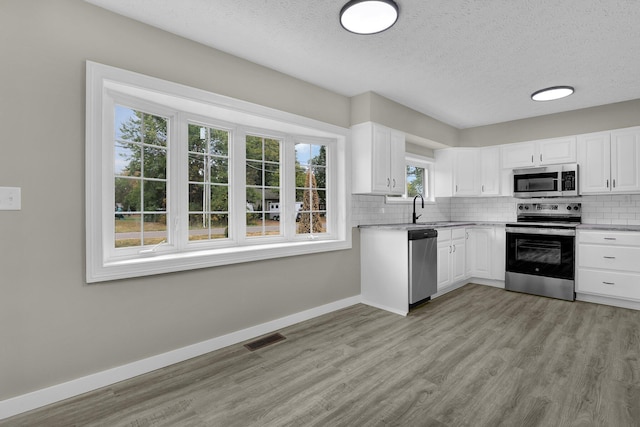 kitchen featuring stainless steel appliances, visible vents, decorative backsplash, light wood-style floors, and a sink