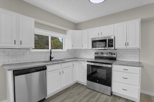 kitchen with stainless steel appliances, light wood-style floors, a sink, and tasteful backsplash