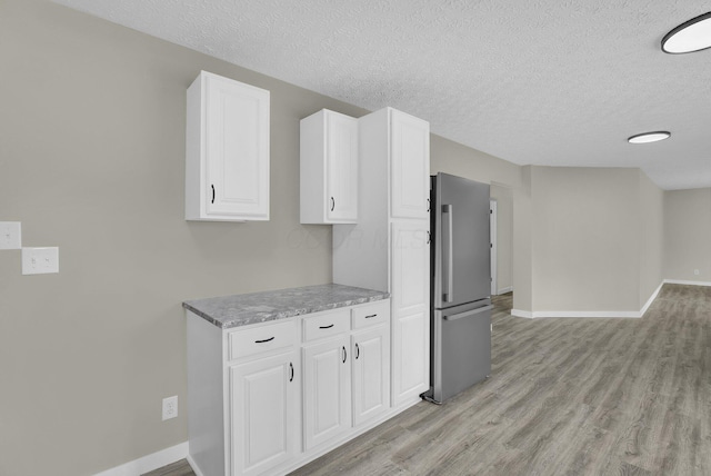 kitchen featuring freestanding refrigerator, white cabinetry, a textured ceiling, light wood-type flooring, and baseboards