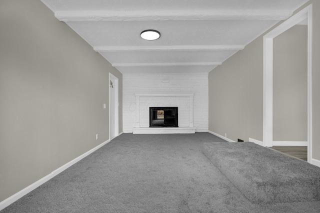 unfurnished living room with a brick fireplace, beam ceiling, baseboards, and dark colored carpet