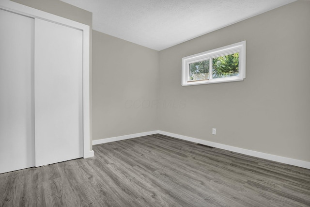 unfurnished bedroom featuring visible vents, a textured ceiling, baseboards, and wood finished floors