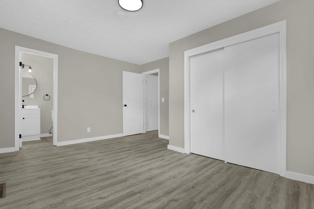 unfurnished bedroom with ensuite bath, a closet, baseboards, and wood finished floors