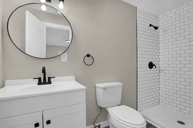 bathroom with a textured ceiling, toilet, vanity, baseboards, and a stall shower