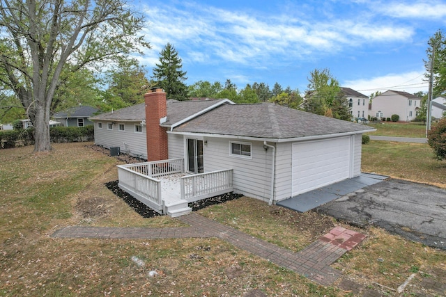 back of property with a lawn, a chimney, roof with shingles, cooling unit, and a wooden deck