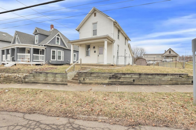 view of front facade featuring covered porch, fence, and a storage unit