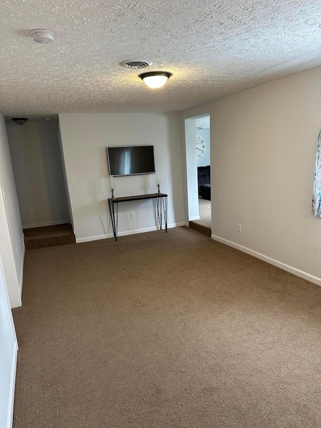 unfurnished living room with a textured ceiling, carpet floors, visible vents, and baseboards