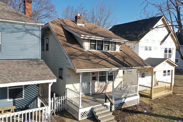 back of house with roof with shingles, a chimney, and a wooden deck