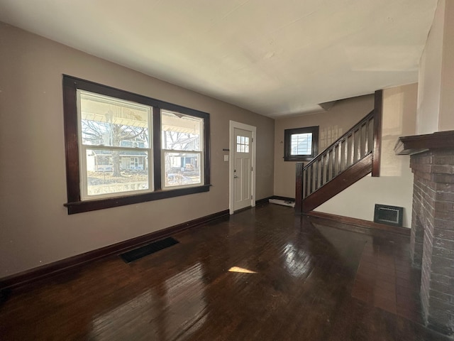 entryway with dark wood-style flooring, a fireplace, visible vents, and baseboards