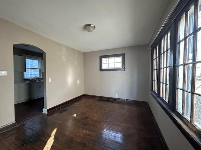 unfurnished room featuring dark wood-style floors, baseboards, arched walkways, and a sink