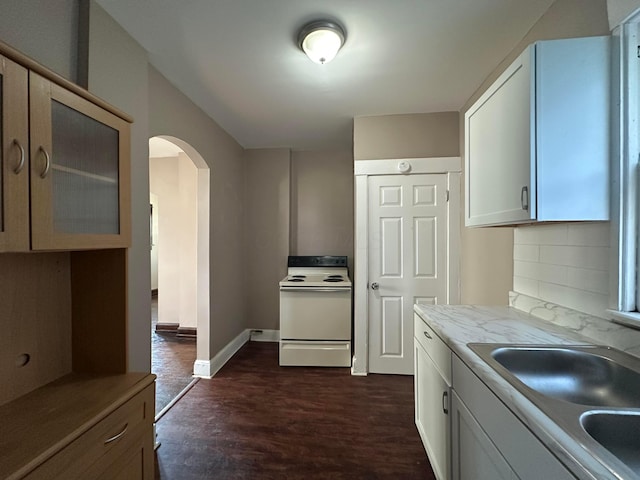 kitchen with white range with electric stovetop, arched walkways, white cabinets, light countertops, and a sink