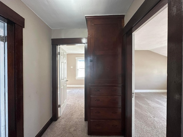 hallway featuring baseboards, vaulted ceiling, and light colored carpet