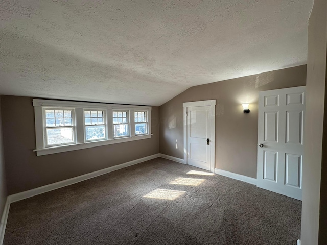 additional living space featuring lofted ceiling, dark colored carpet, a textured ceiling, and baseboards