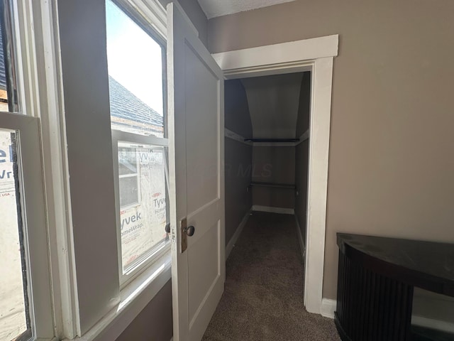 corridor featuring dark colored carpet and baseboards