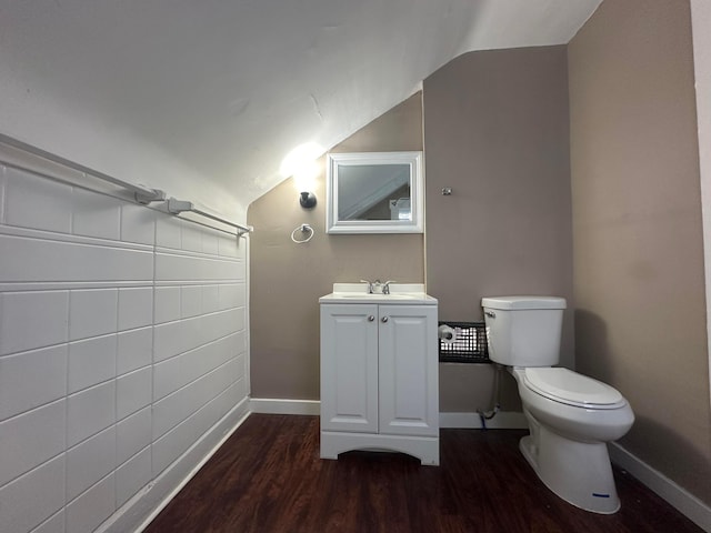 half bath with toilet, vaulted ceiling, vanity, wood finished floors, and baseboards