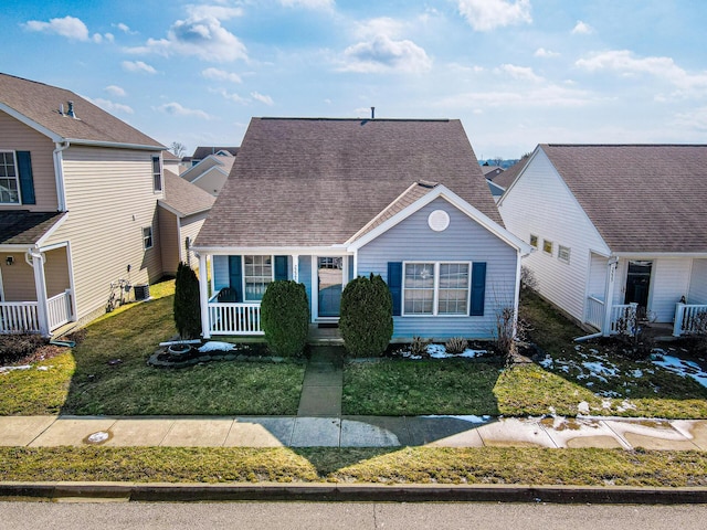 view of front facade with a porch, roof with shingles, a front yard, and a residential view