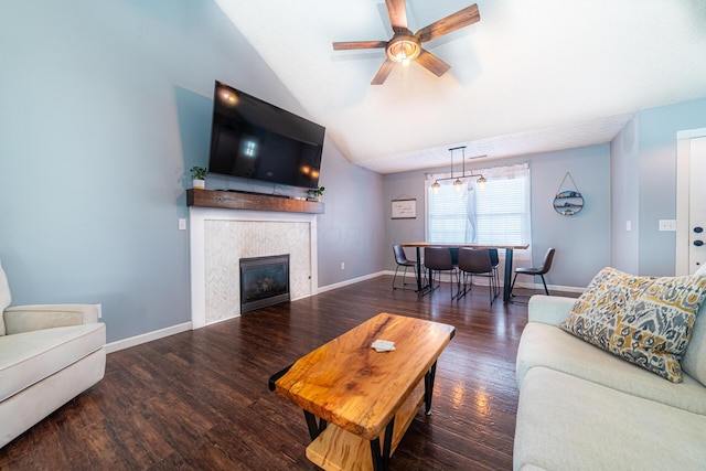 living area featuring a fireplace, dark wood-type flooring, a ceiling fan, vaulted ceiling, and baseboards