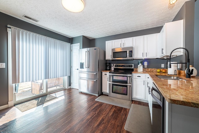 kitchen with visible vents, white cabinets, dark wood finished floors, stainless steel appliances, and a sink