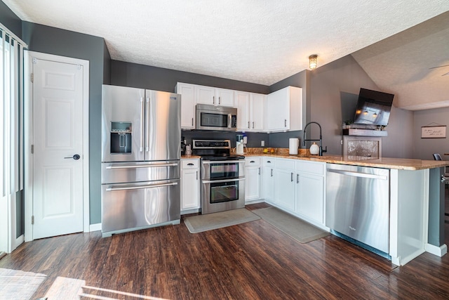 kitchen with stainless steel appliances, a peninsula, dark wood finished floors, and white cabinetry