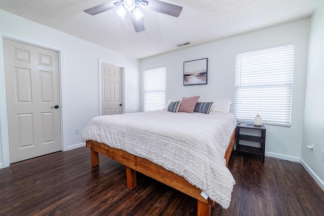 bedroom with dark wood-style floors, visible vents, a textured ceiling, and baseboards