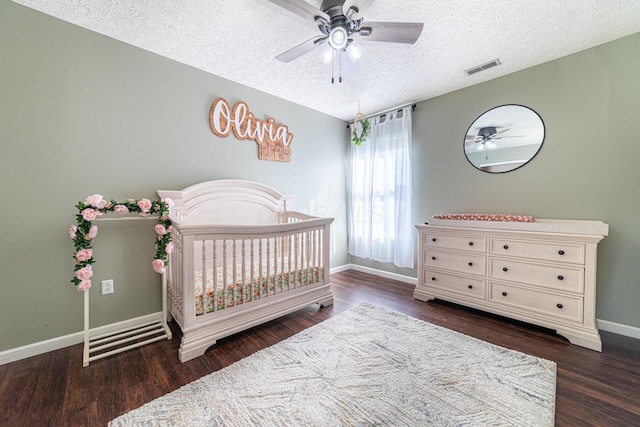 bedroom featuring dark wood-style flooring, visible vents, a textured ceiling, a nursery area, and baseboards