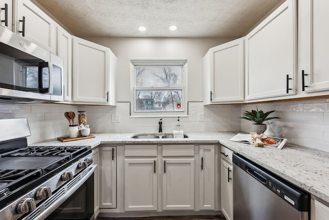 kitchen featuring appliances with stainless steel finishes, white cabinetry, a sink, and light stone counters