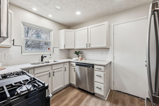 kitchen featuring light wood finished floors, white cabinets, appliances with stainless steel finishes, light stone countertops, and a sink