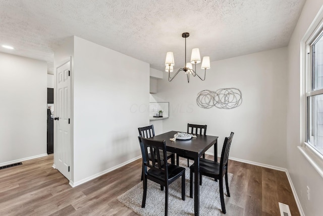 dining room featuring a textured ceiling, wood finished floors, visible vents, and baseboards