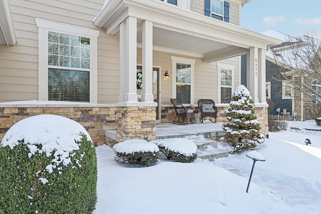 snow covered property entrance with stone siding and covered porch