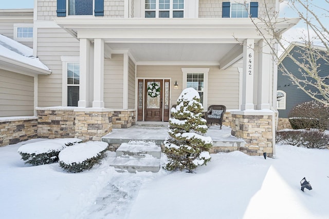 snow covered property entrance featuring stone siding