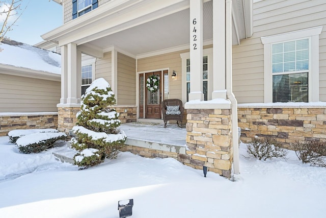 snow covered property entrance with stone siding and covered porch