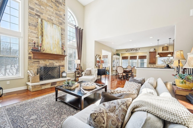 living room with plenty of natural light, a stone fireplace, baseboards, and wood finished floors