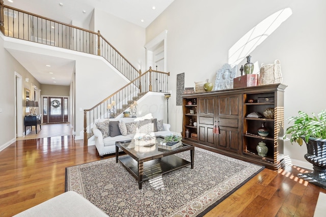 living area with recessed lighting, a high ceiling, wood finished floors, baseboards, and stairway