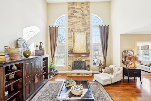 living area featuring a wealth of natural light, a stone fireplace, a towering ceiling, and wood finished floors