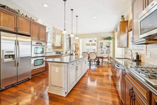 kitchen featuring appliances with stainless steel finishes, brown cabinetry, a kitchen island, and hanging light fixtures