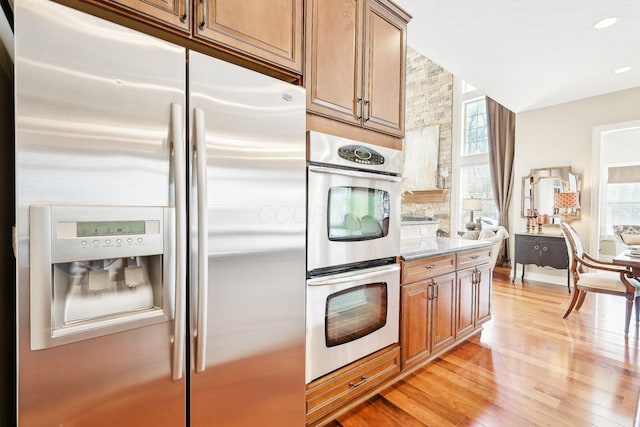 kitchen featuring light wood-type flooring, plenty of natural light, appliances with stainless steel finishes, and brown cabinets