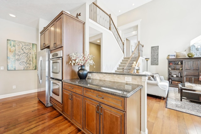 kitchen with stainless steel appliances, dark wood-type flooring, open floor plan, brown cabinets, and dark stone countertops