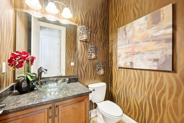 half bathroom with baseboards, vanity, and toilet