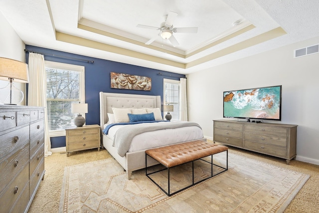 bedroom with a tray ceiling, light colored carpet, visible vents, a ceiling fan, and baseboards