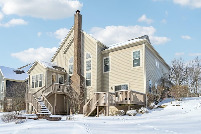 snow covered back of property with stairs, a chimney, and a wooden deck