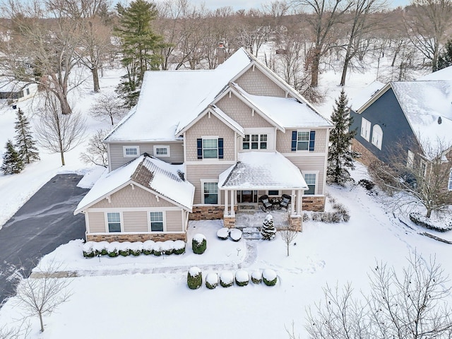 snow covered house featuring a garage and stone siding