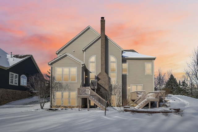 snow covered property with a chimney, a wooden deck, and stairs