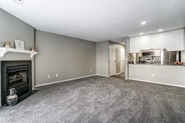 unfurnished living room featuring dark carpet, a fireplace with flush hearth, and baseboards