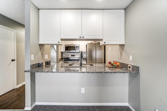 kitchen with stainless steel appliances, dark stone counters, white cabinets, and a sink