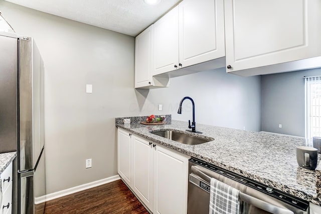 kitchen featuring dark wood finished floors, appliances with stainless steel finishes, white cabinetry, a sink, and light stone countertops